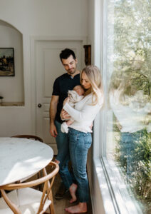Austin Newborn Photographer, mother and father standing with newborn baby next to large window