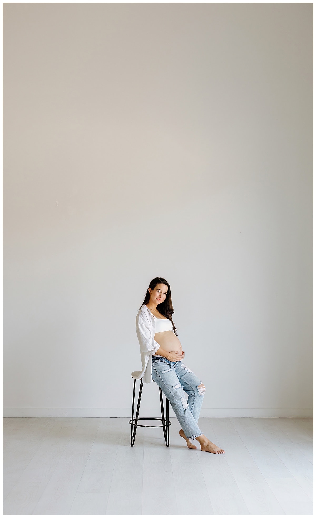 Woman sits on stool embracing belly for Studio Maternity Photos