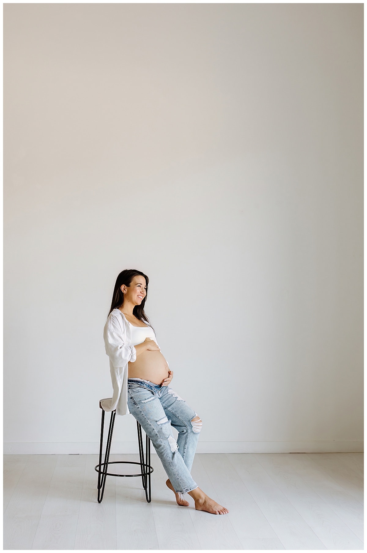 Adult sits on stool holding pregnant belly for Our Adventuring Souls Photography