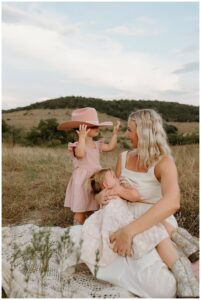 Mom lays down on grassy field with daughters for Austin Lifestyle Photographer