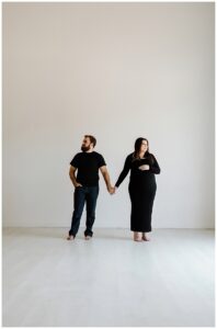 Couple holds hands together during her studio maternity session