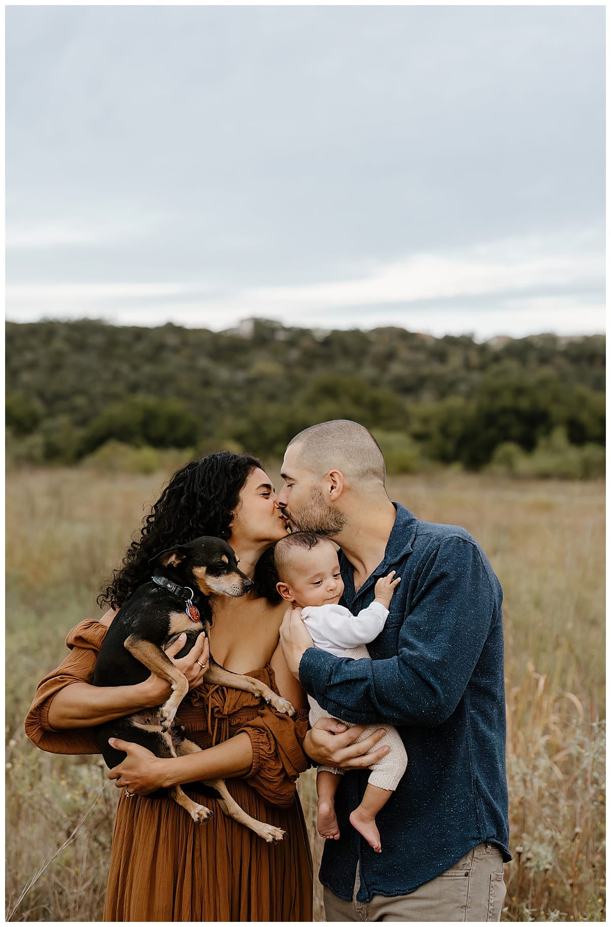 Parent share a kiss holding their son and dog or Our Adventuring Souls Photography
