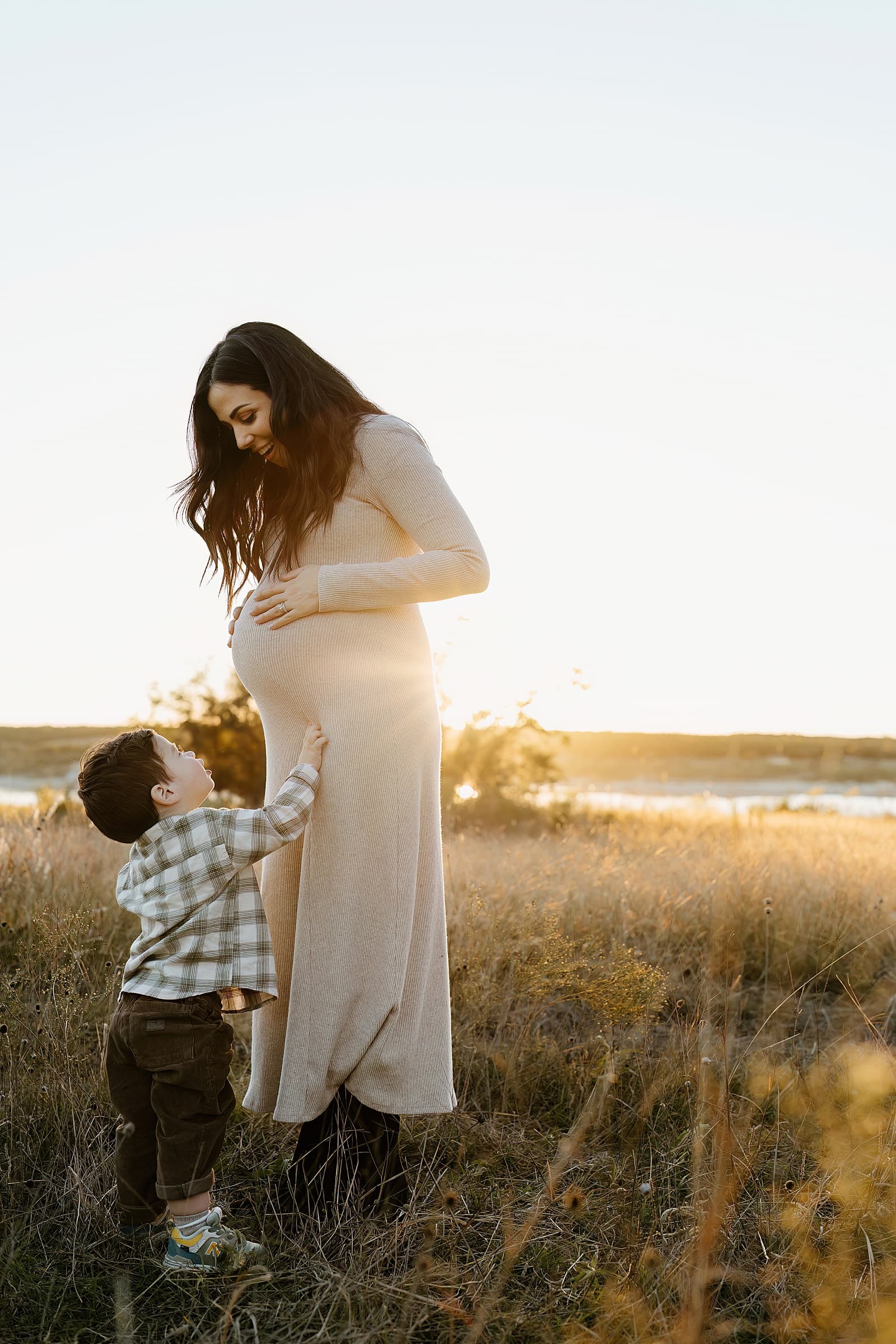 Son smiles up at moms pregnant belly during an Outdoor Lifestyle Maternity Session