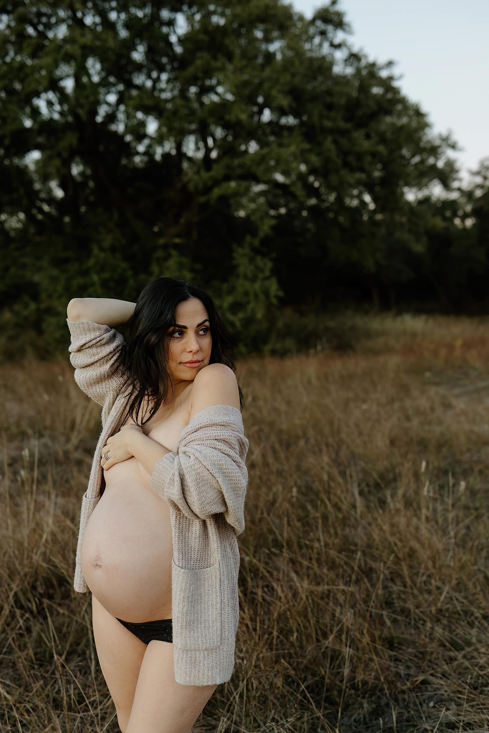 Woman covers chest and stands outside with pregnant belly for Austin Motherhood Photographer