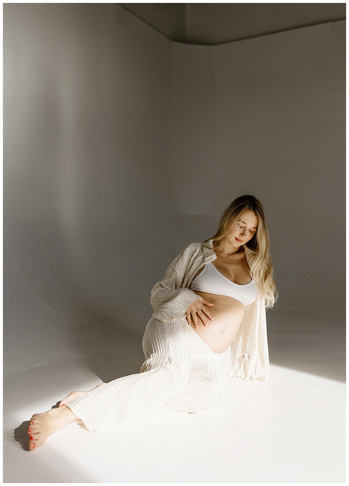 Adult sits on the floor during her studio maternity session